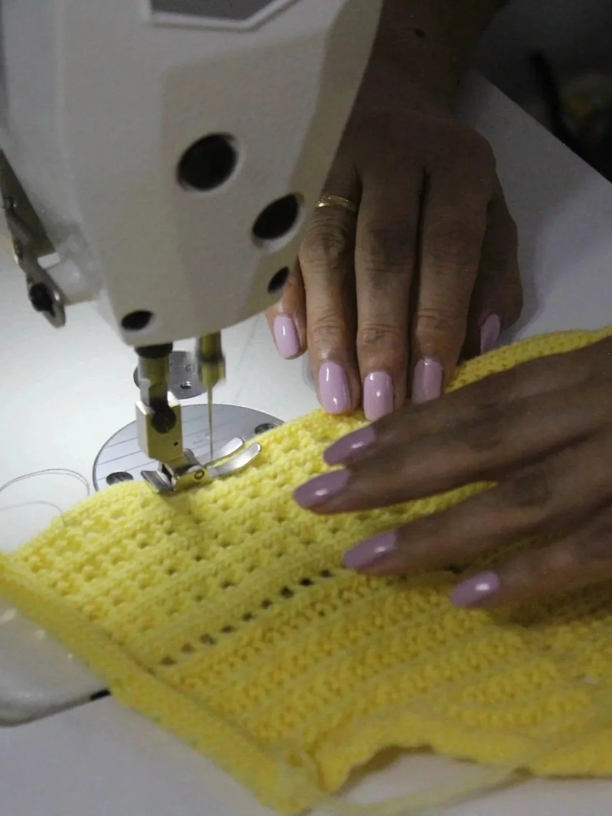 Close-up of hands guiding yellow fabric under a sewing machine needle.