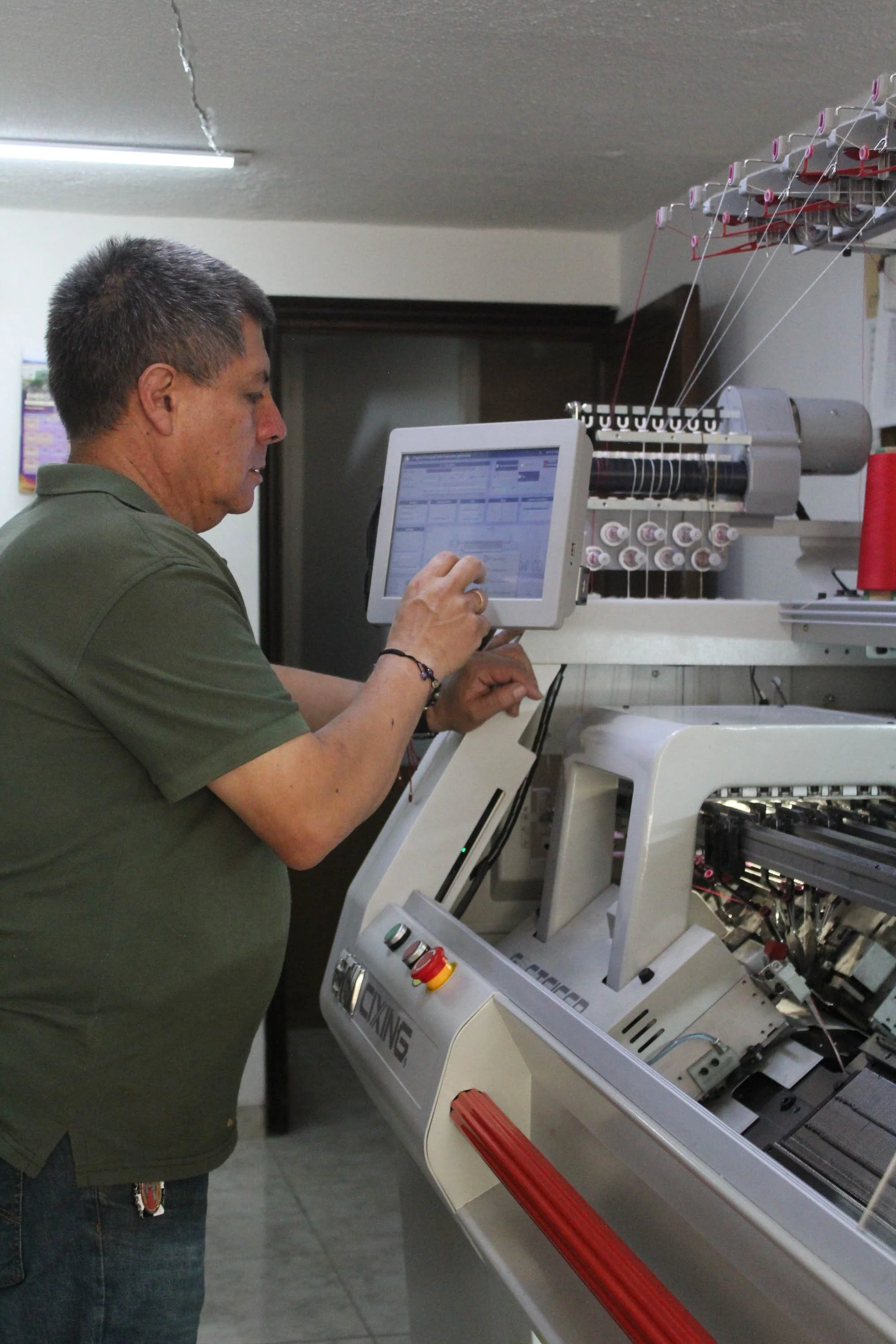 A man working on an industrial embroidery machine with a digital touchscreen controller.