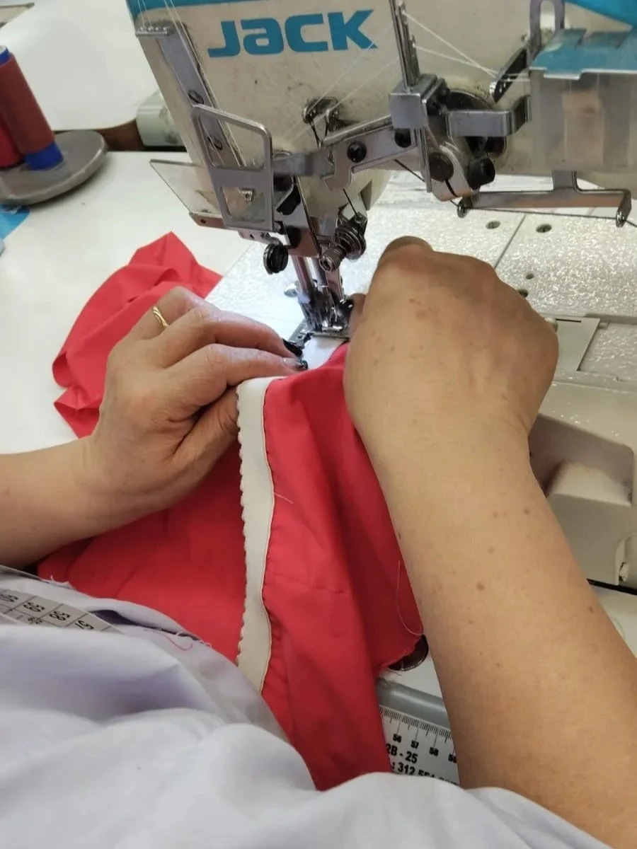 Person sewing a red piece of fabric using a sewing machine.