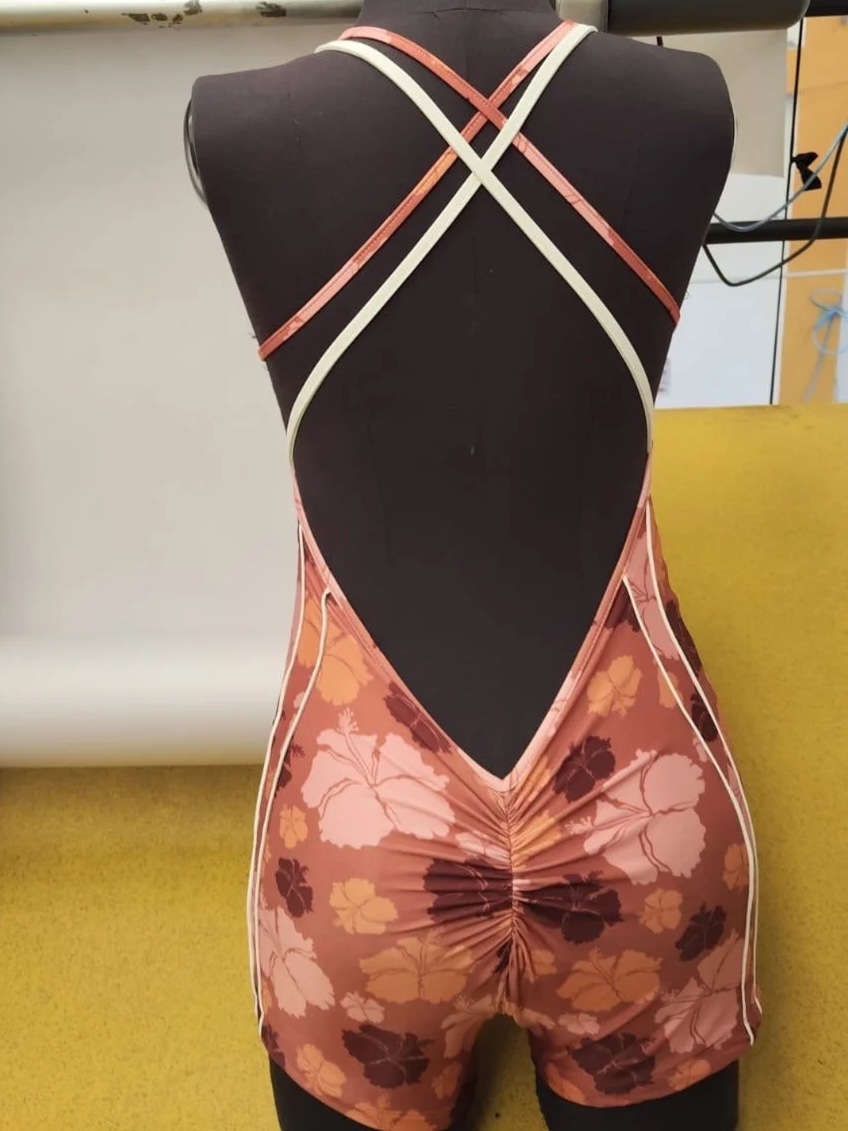A black mannequin wearing a floral-patterned swimsuit with crisscross straps on the back and ruched fabric on the lower back area.