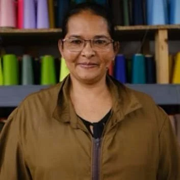 A woman standing indoors in front of shelves filled with colorful fabric bolts.