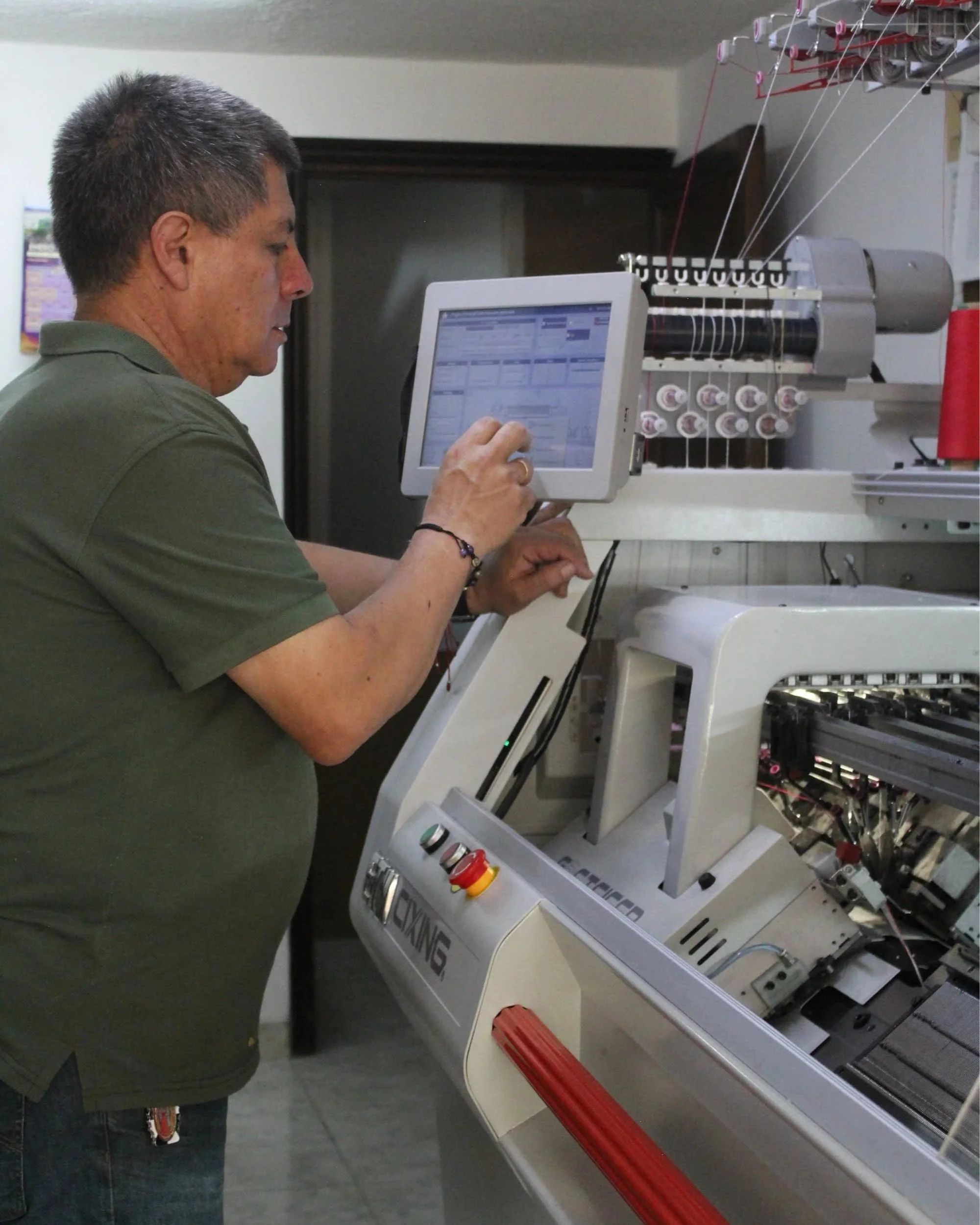 Man operating a machine with a computer monitor in a workshop or factory setting.