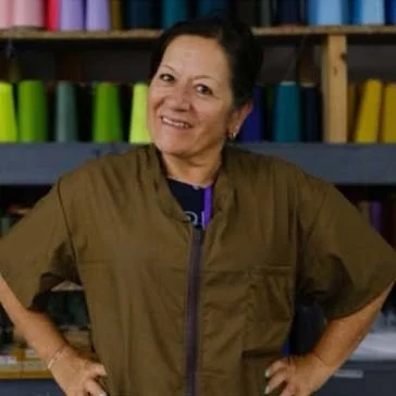 A woman with short dark hair smiling, wearing a brown jacket, standing in front of shelves filled with colorful binders.