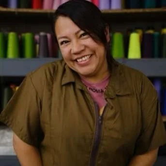 A woman smiling in front of shelves with colorful spools of thread.