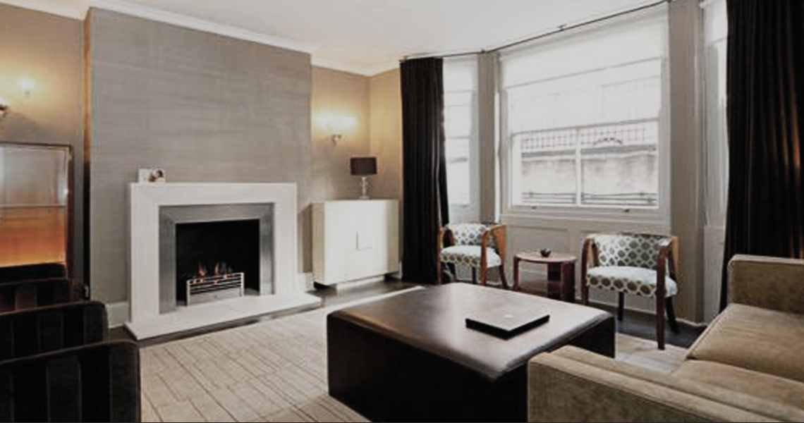 Sitting room with bronze silk wallpaper, limestone fire, bespoke TV cabinet in parchment, Murano lights, bespoke rug, and art deco chairs