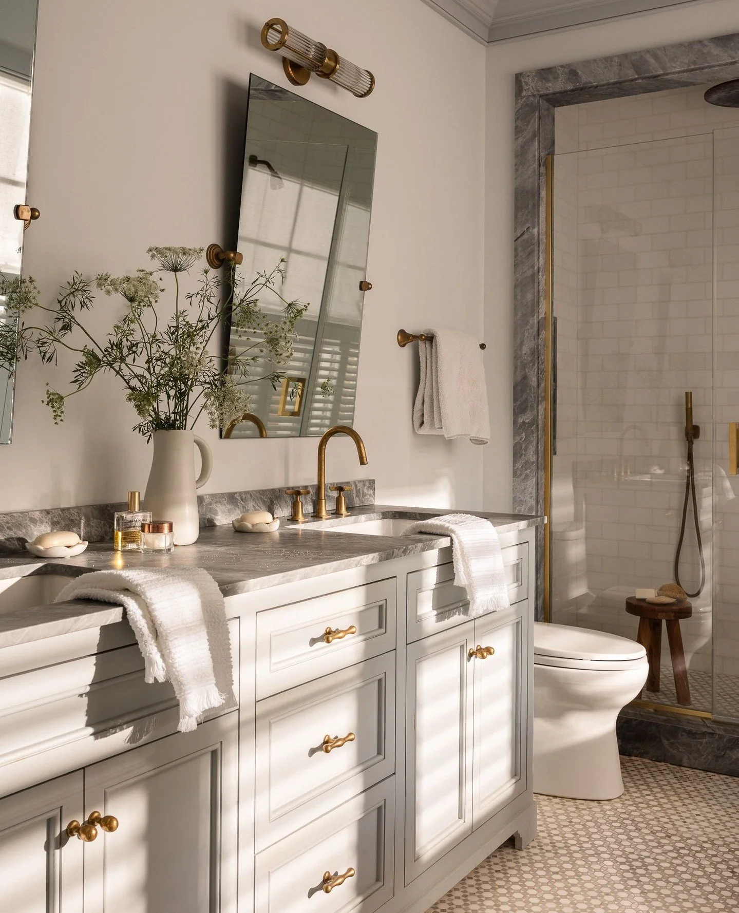 Soft northeastern light filters into the primary bathroom each morning, catching the brass fixtures and veined marble in a warm, reflective glow. Designed in collaboration with Sara Gilbane, the palette of pale cabinetry and natural stone evokes calm