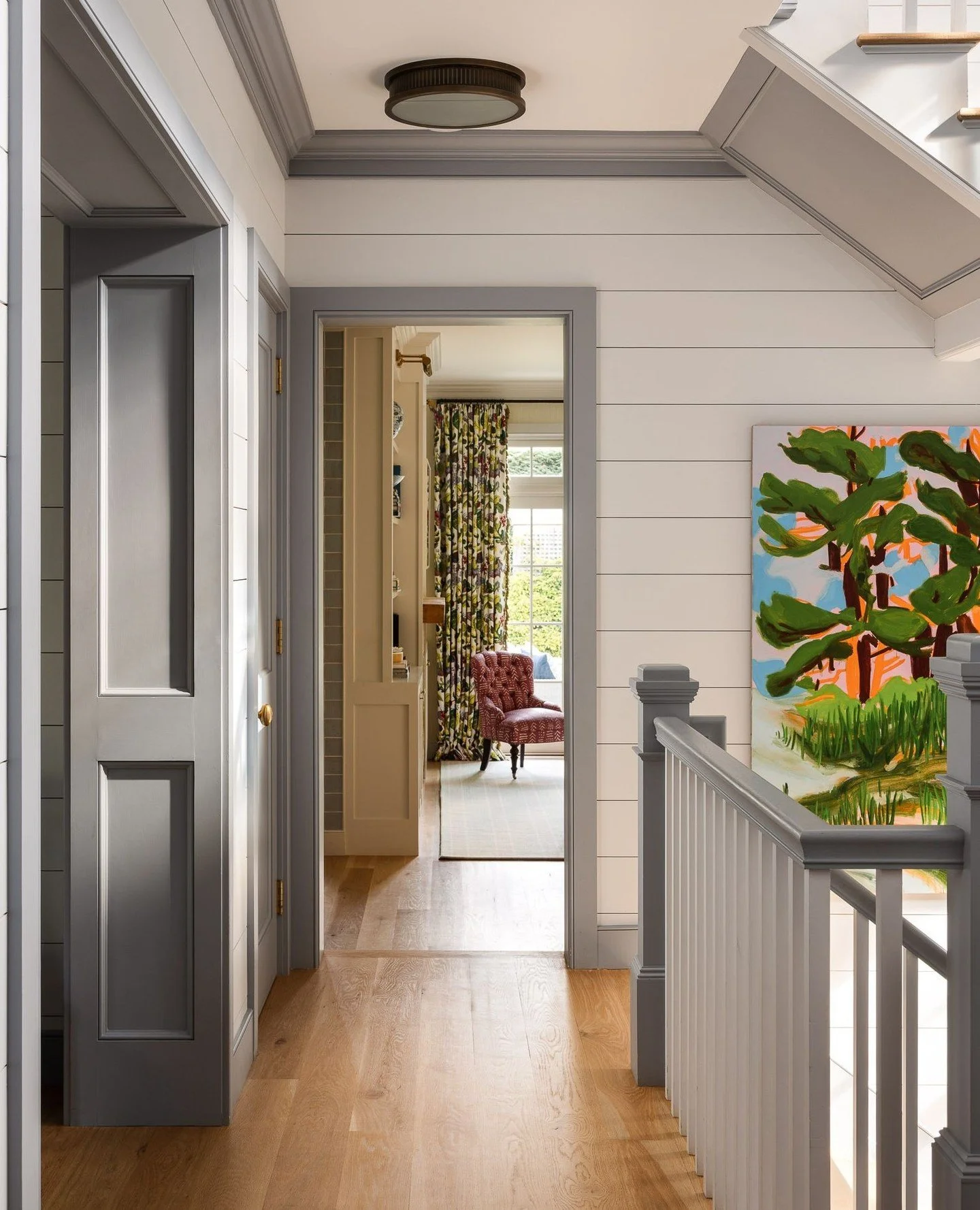 From the stair hall, a view unfolds toward the living room at the rear of the home. To the left, the paneled foyer opening adds depth and proportion, while light from the three-story west-facing glass wall fills the corridor with a soft glow througho