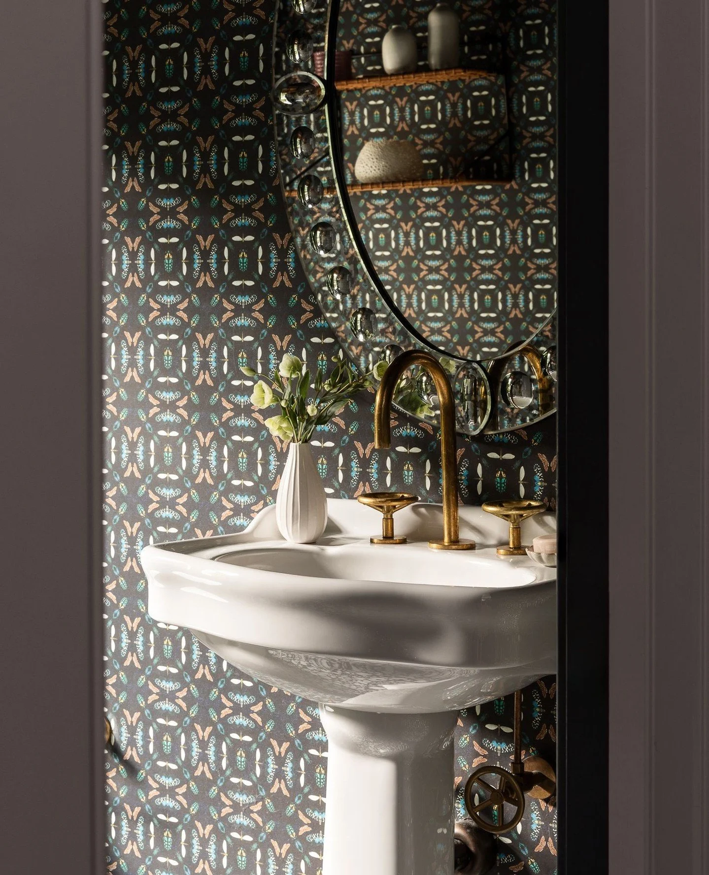 Tucked just off the stair hall, the powder room is quietly set apart from the home&rsquo;s main gathering spaces. Natural light filters through a private west-facing window, illuminating the unlacquered brass fittings and patterned walls that bring c