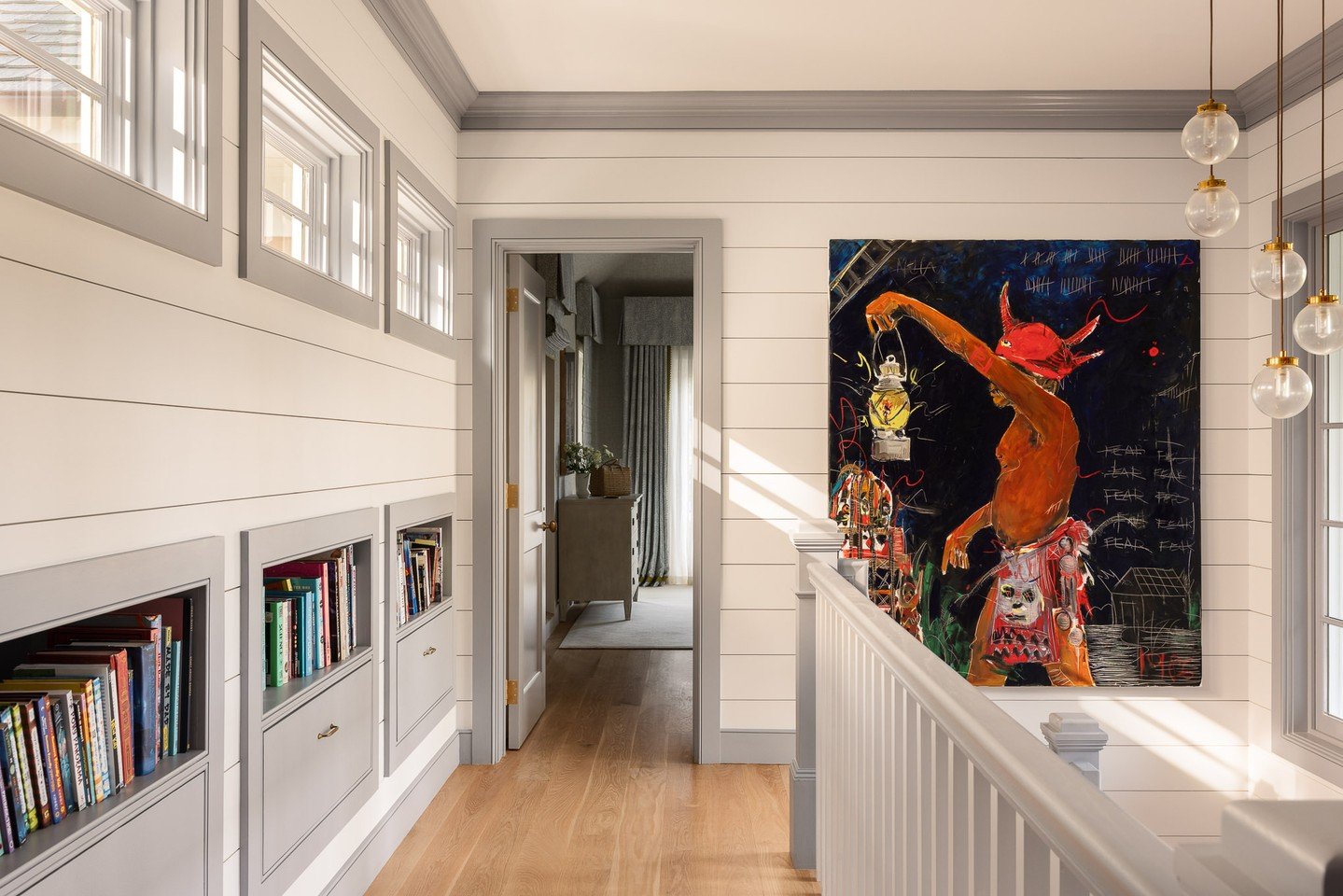 Built-in shelving and drawers tuck neatly beneath the portico roofline, turning every inch of space into purposeful storage. Natural light from the stair&rsquo;s west-facing windows filters across painted shiplap walls, animating the art and architec