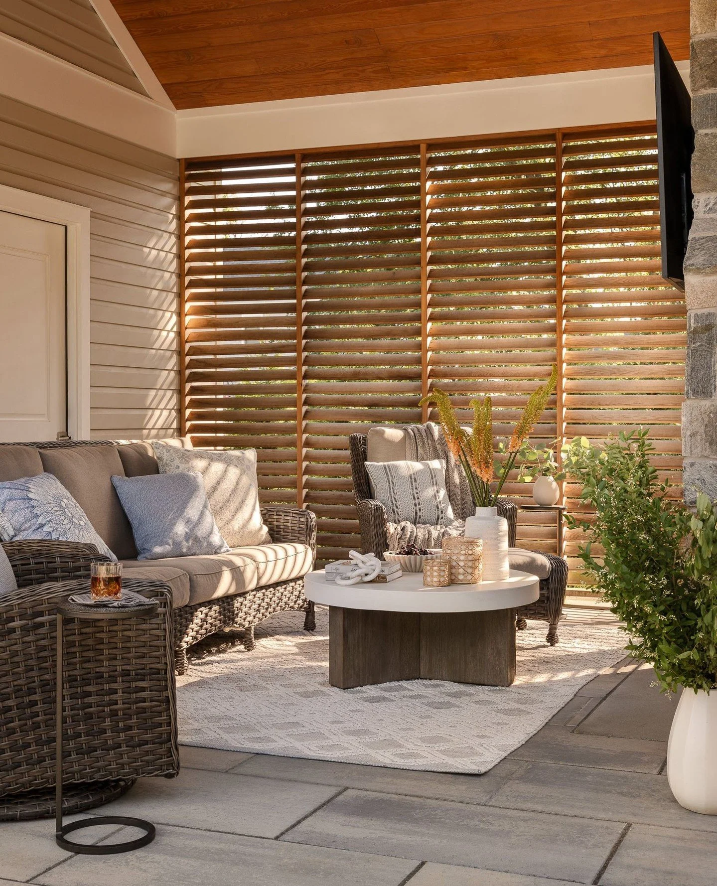 Cedar tongue-and-groove overhead, lattice panels at the edge&mdash;this covered lounge balances openness with enclosure. Woven furnishings, soft textiles, and filtered light create a layered comfort that shifts easily from summer afternoons to autumn