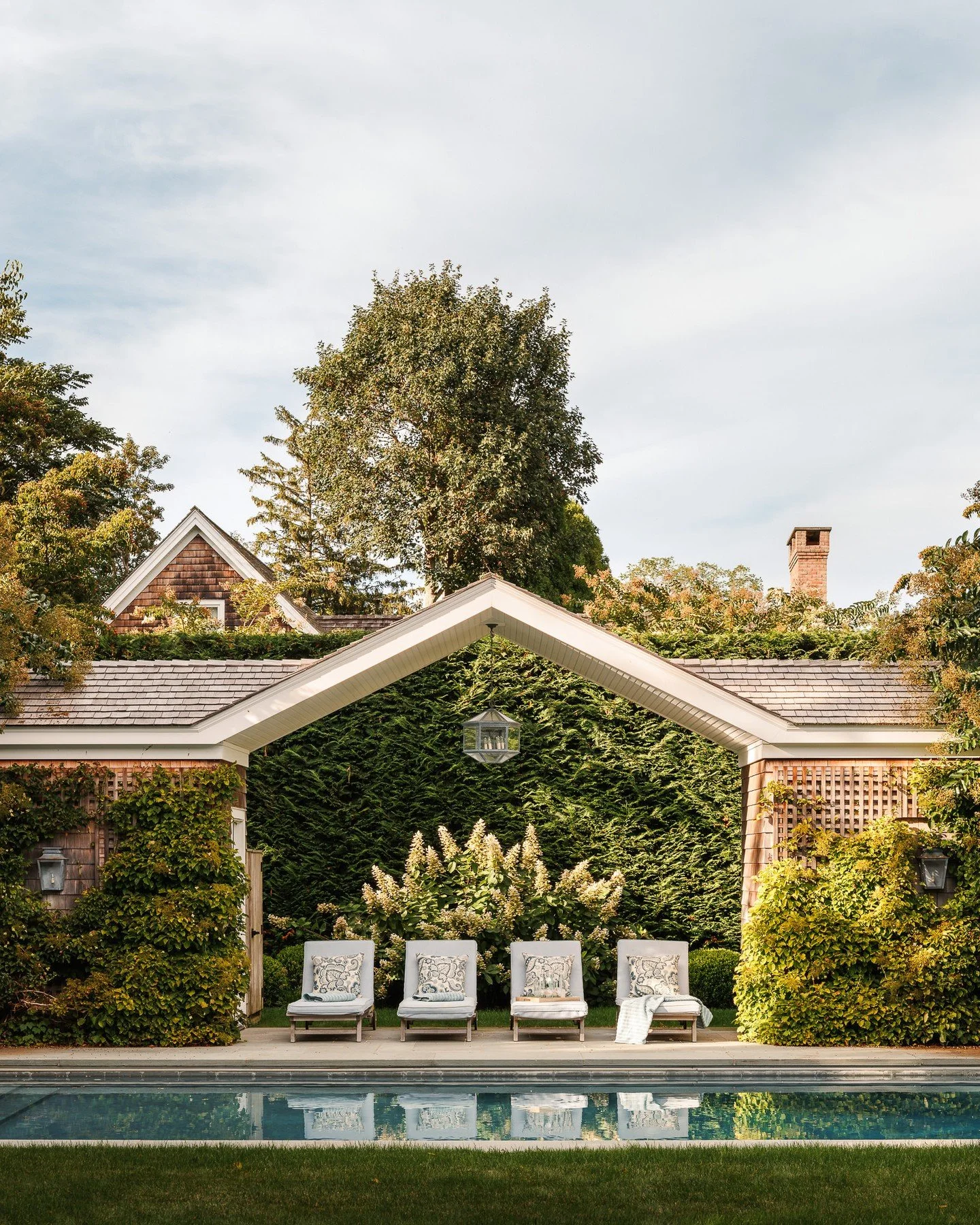 At the far end of the pool, a gabled arbor joins two cedar-clad pavilions&mdash;one housing the bath and pool equipment, the other for storage. The symmetry and axial alignment with the main house create a quiet focal point, where geometry, greenery,