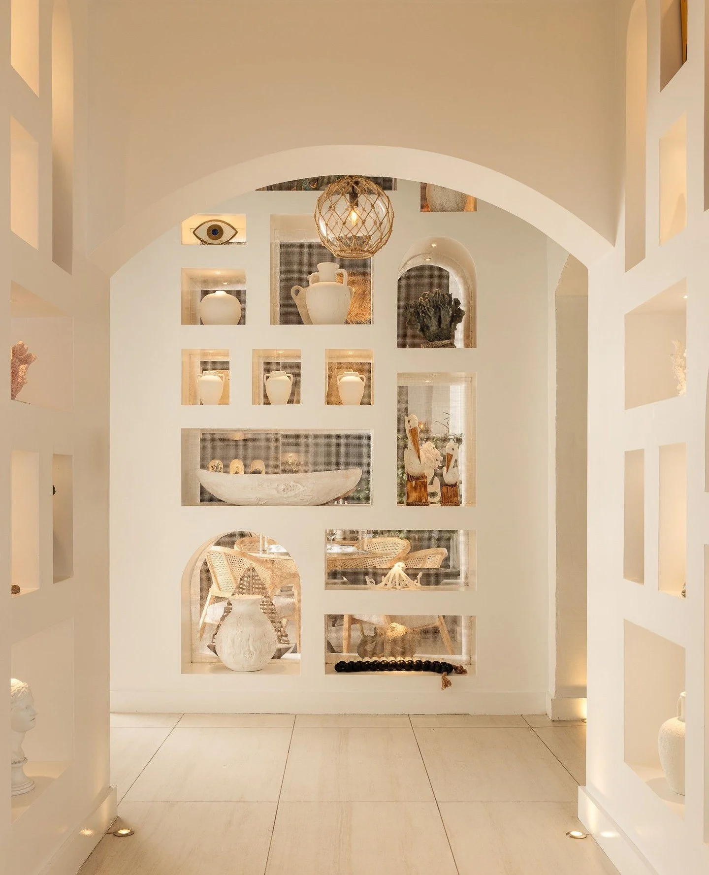 The first impression at Trata unfolds through an arched threshold into a luminous wall of illuminated niches. Sculptural vessels, coral forms, and classical fragments are framed within softly glowing recesses, creating depth and symmetry from the mom