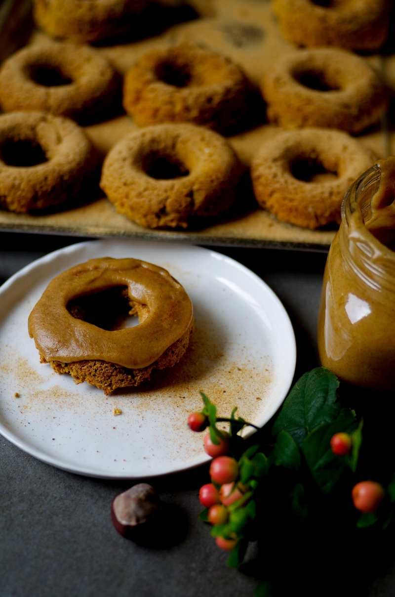 Salted caramel sauce on a baked pumpkin chai spiced donut; cinnamon vanilla sprinkle dusted donuts in background.