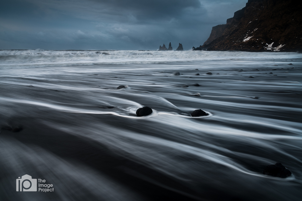 water rushes over rocks on black sand beach stormy day in vik south iceland by nathan barry the image project