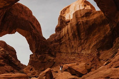 Couple standing under double arch in Arches National Park