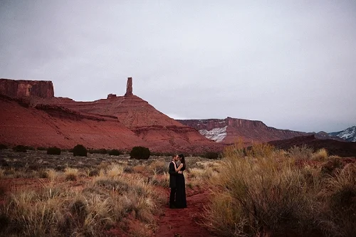 Couple stands near red rock in Southern Utah at their engagement shoot