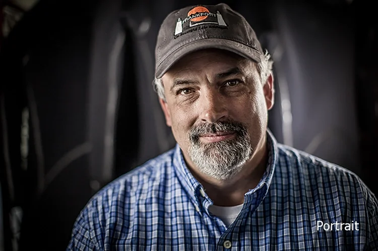 A middle-aged man with a beard wearing a baseball cap and a blue checkered shirt, looking at the camera with a slight smile.