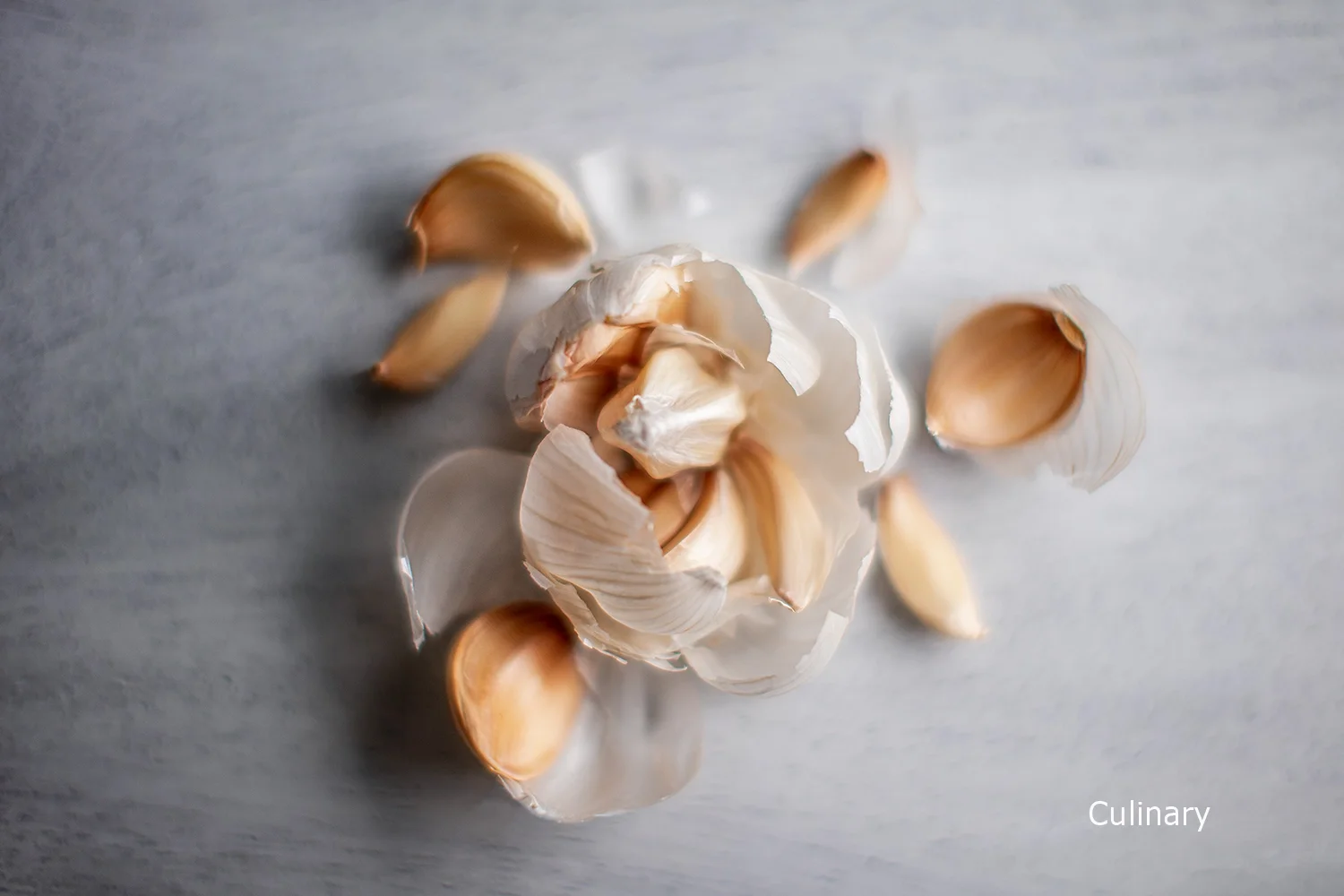 Clove of garlic with some separated garlic cloves on a light-colored surface.