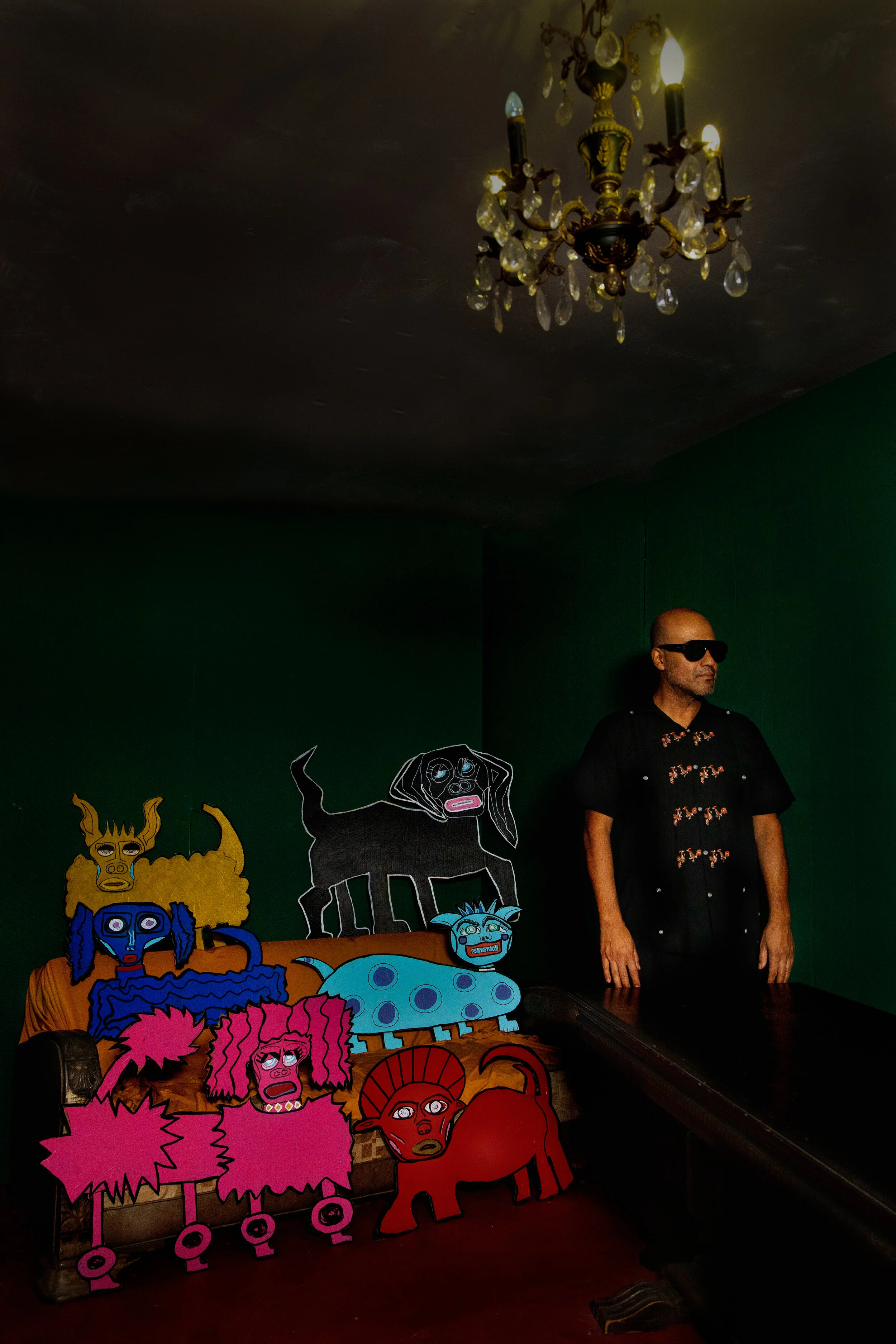 Juan Escobedo standing beside The Puppy Chulos, a collection of colorful illustrated animal and fantasy characters, in an interior art installation.