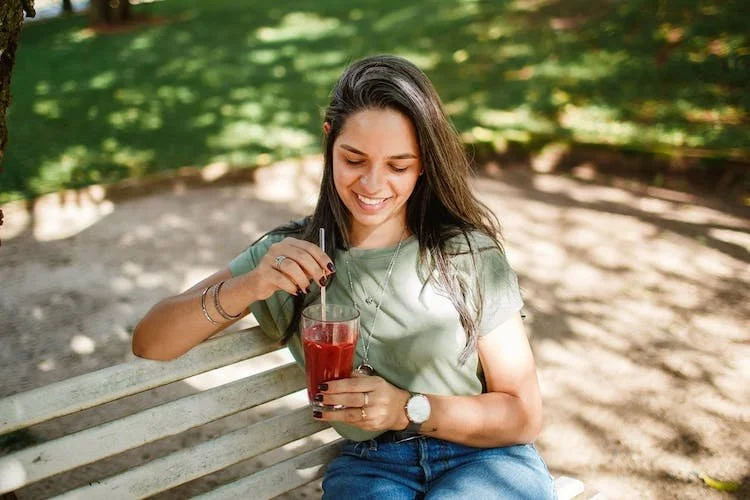 woman sitting on a park bench and drinking juice.