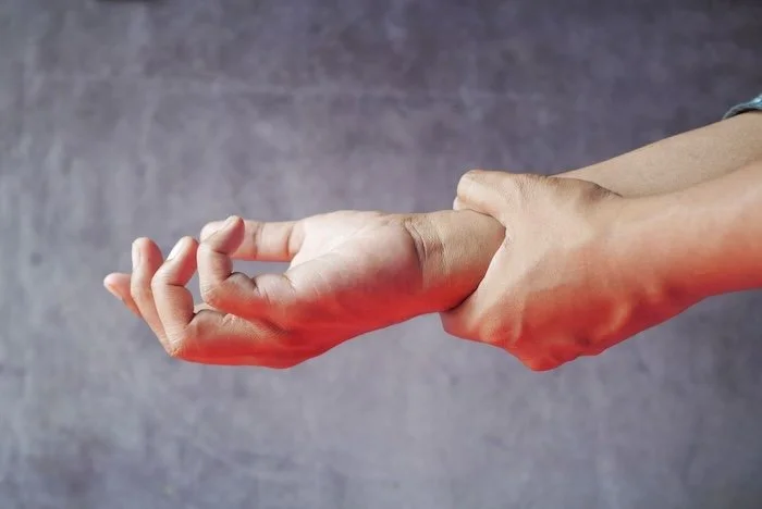 Close-up of hands, one grasping the other, symbolizing pain or discomfort