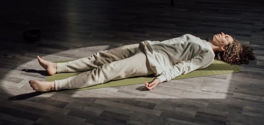 Woman lying on a yoga mat indoors, meditating and relaxing in a calm setting.
