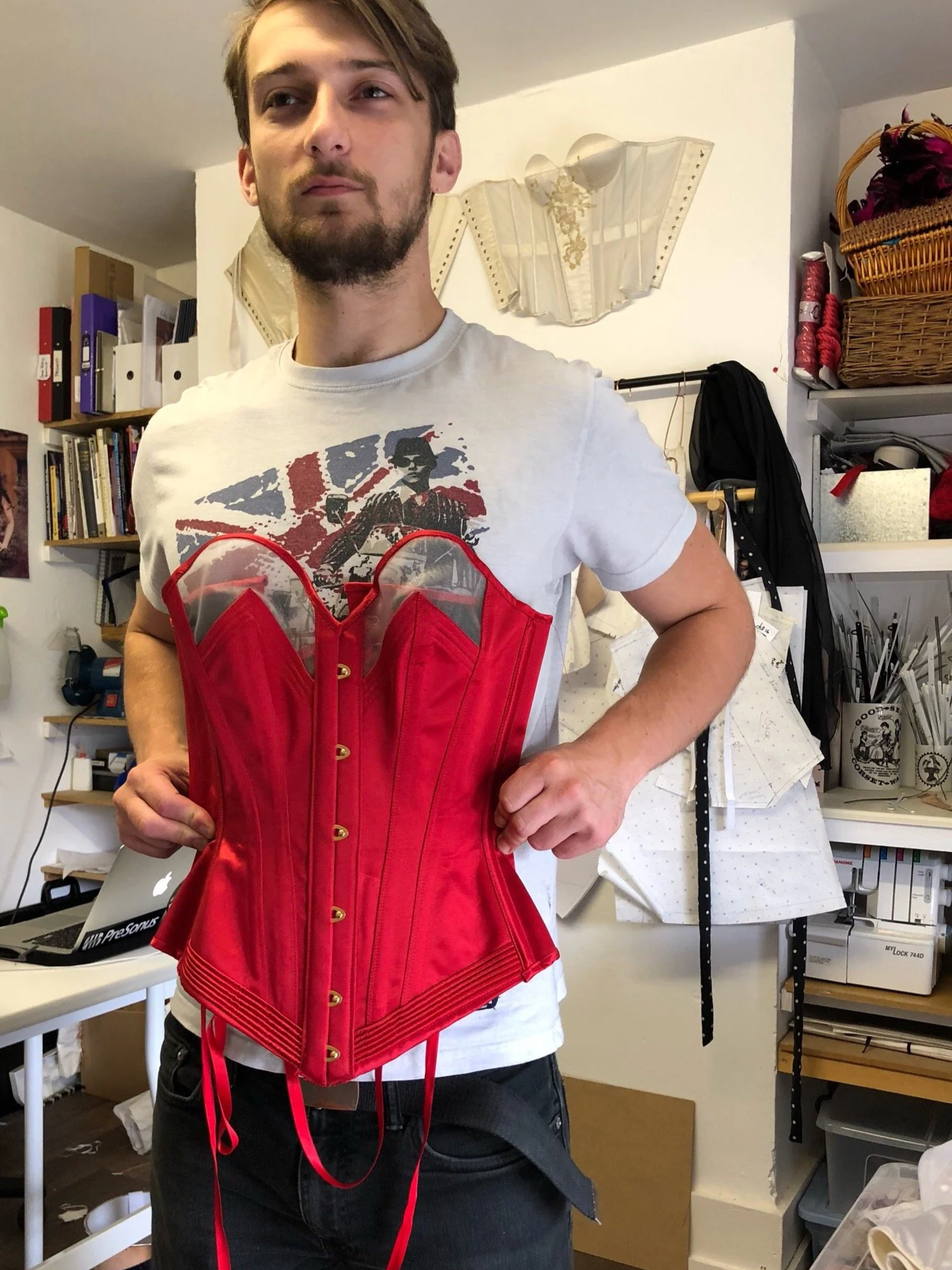 A man holding a female corset to his torso demonstrating that male bodies are generally longer than female bodies