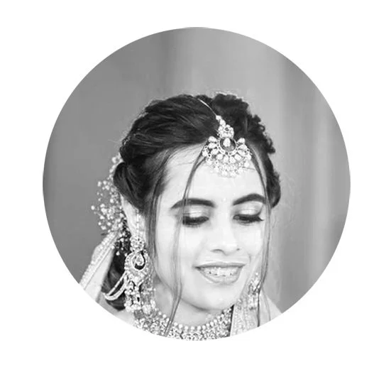 Black and white portrait of a woman wearing traditional jewelry, including a maang tikka and earrings, smiling.