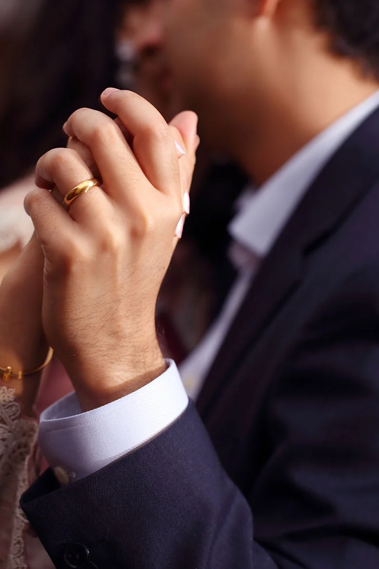 Close-up of a couple holding hands, focus on hands with wedding rings and man in a suit.