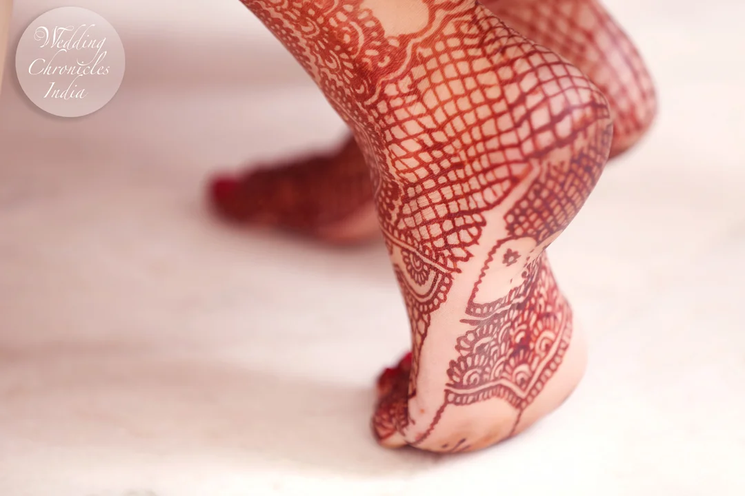 Feet with intricate henna designs on a marble floor.