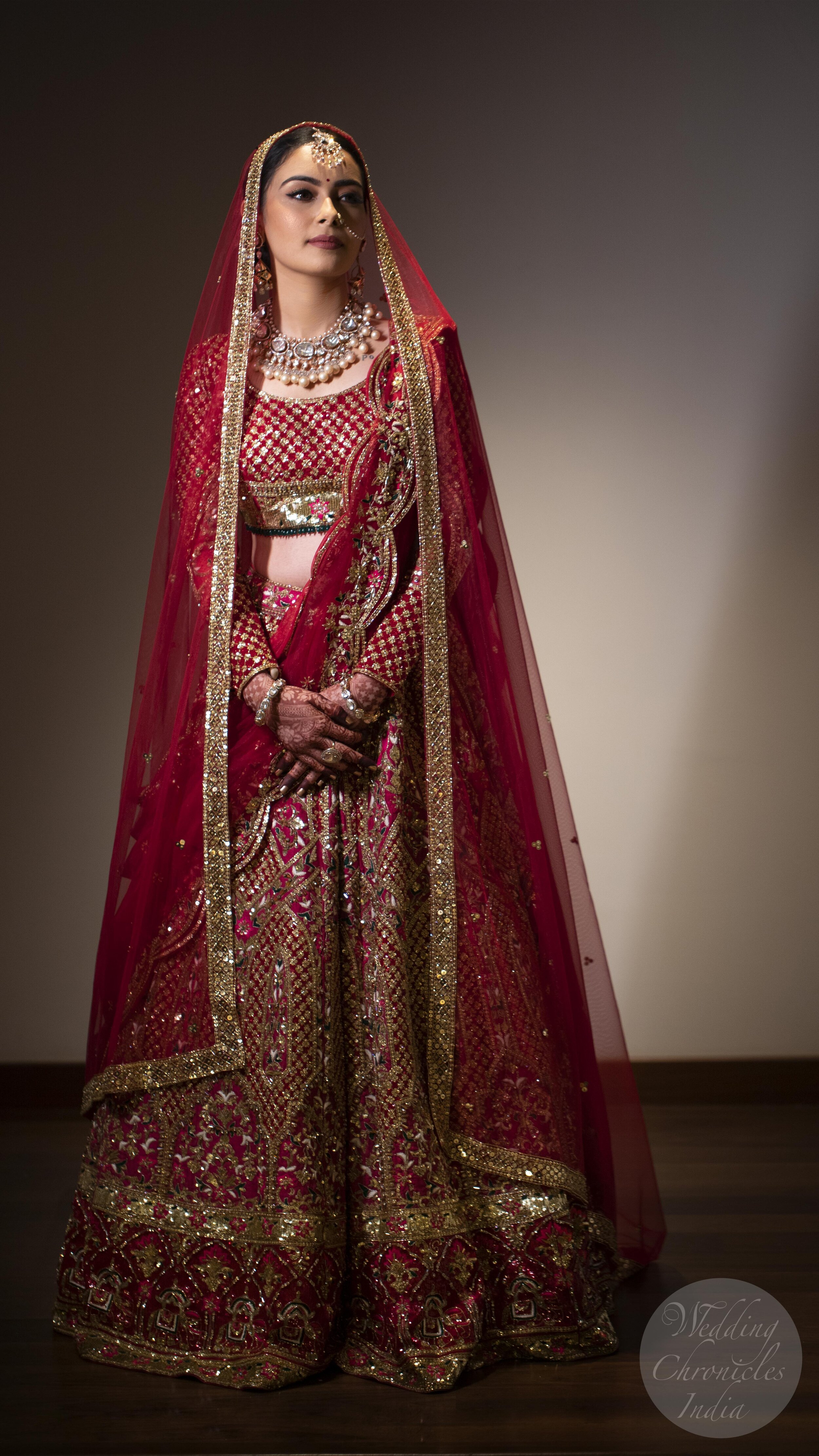 Bride in traditional red and gold Indian bridal attire with intricate jewelry and henna.