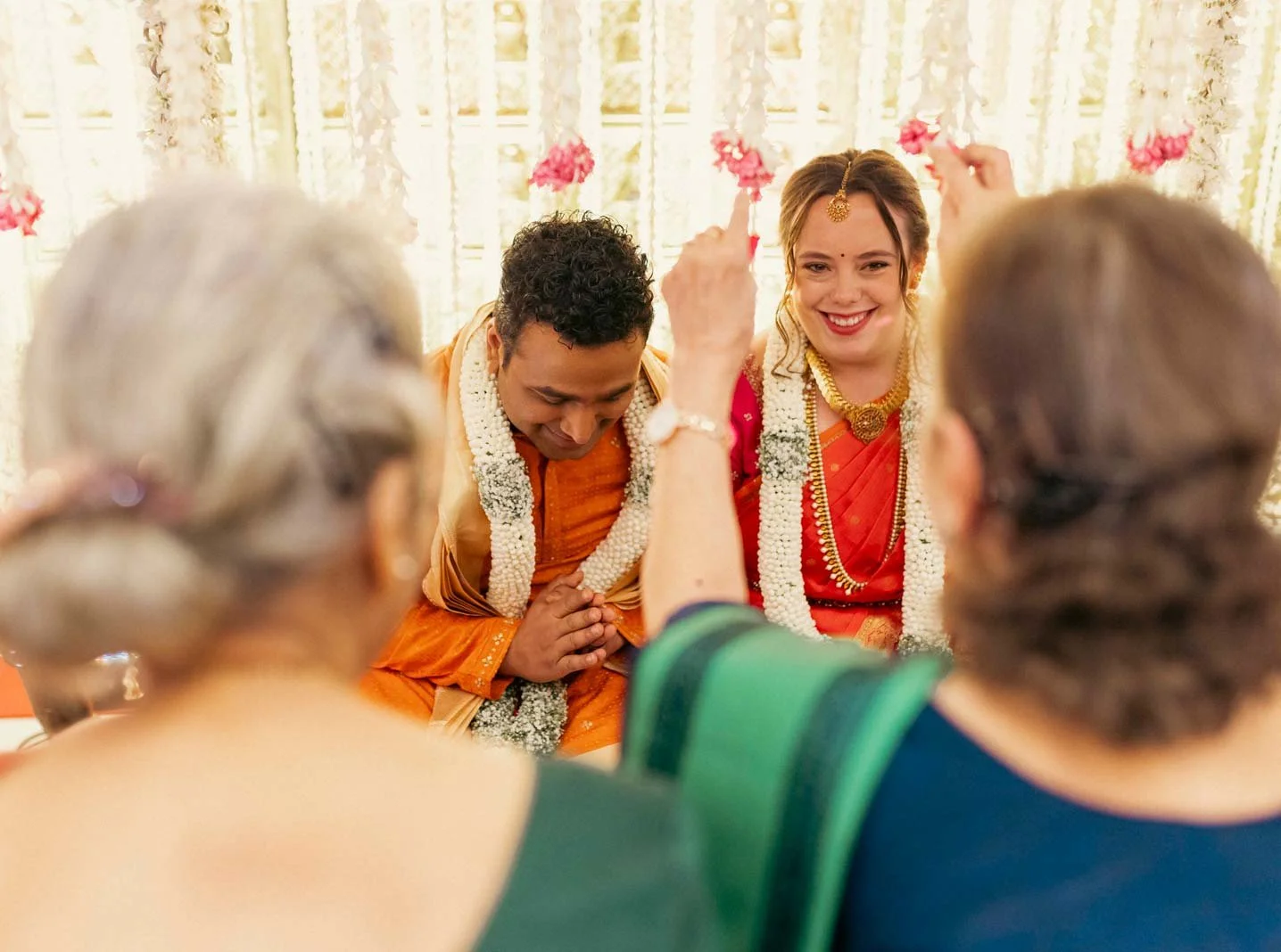 Candid moment as guest greets and blesses by showering flowers on groom and bride in traditional oonjal ceremony in South Indian Wedding

