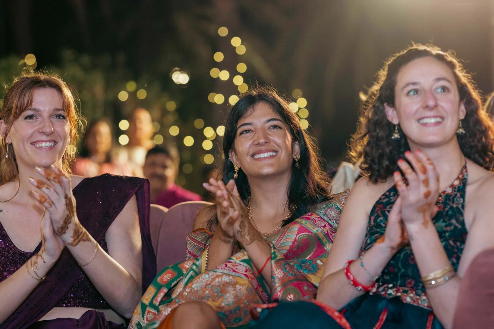 Candid photo of a lady as she looks on and smiles during Sangeeth dance performance of the groom with his friends in Indian Wedding