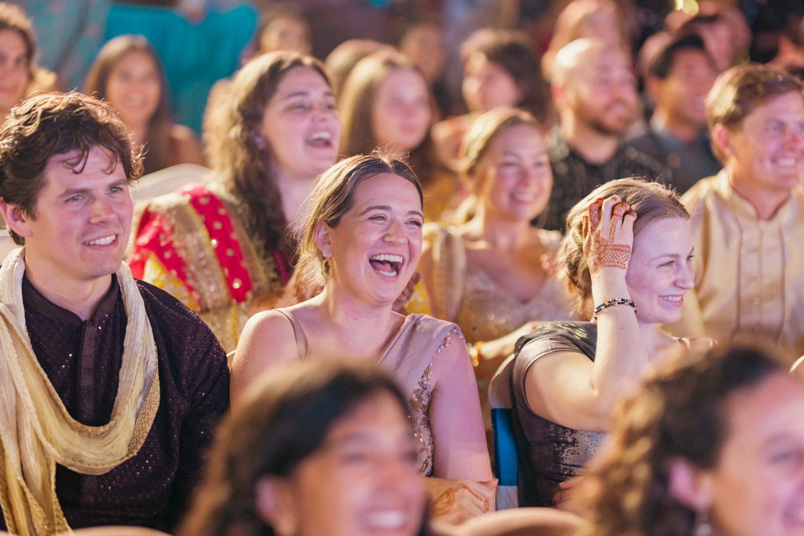 Candid photo of a lady in the audience as she laughs during Sangeeth dance performance of the groom with his friends in Indian Wedding
