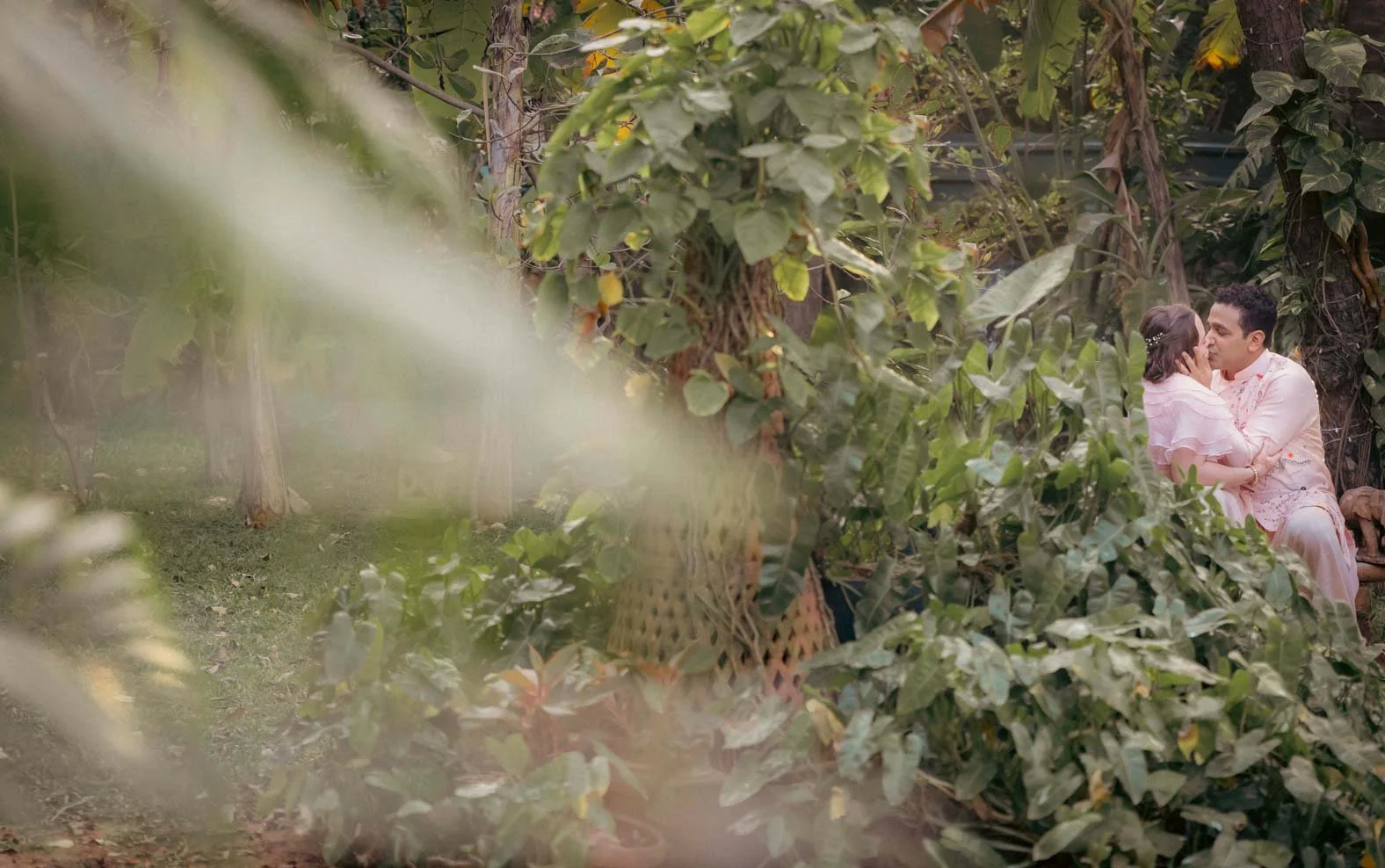 Intimate photo of a couple kissing in a lush green background during their wedding ceremony