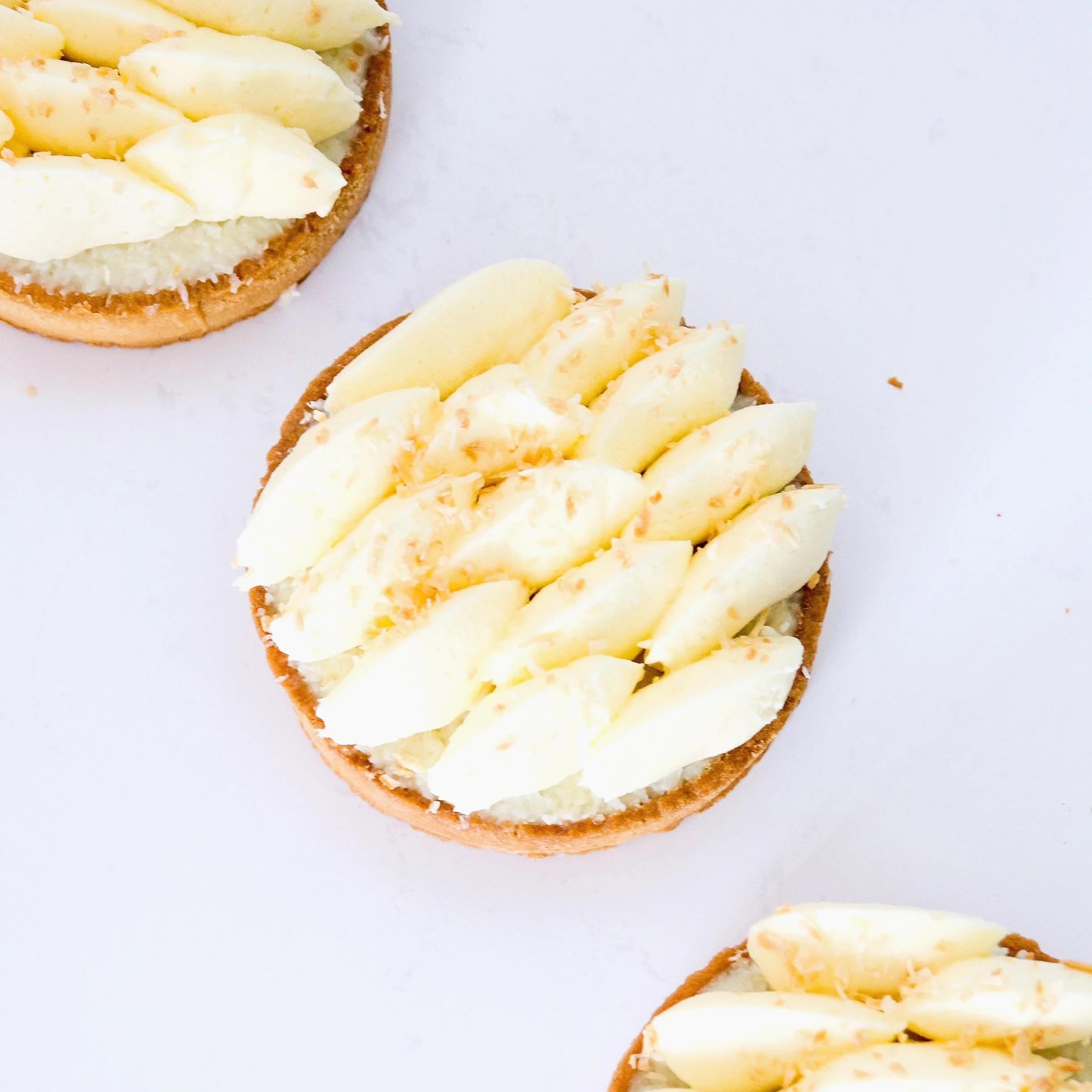 Close-up of three tartlets topped with sliced bananas on a white background.