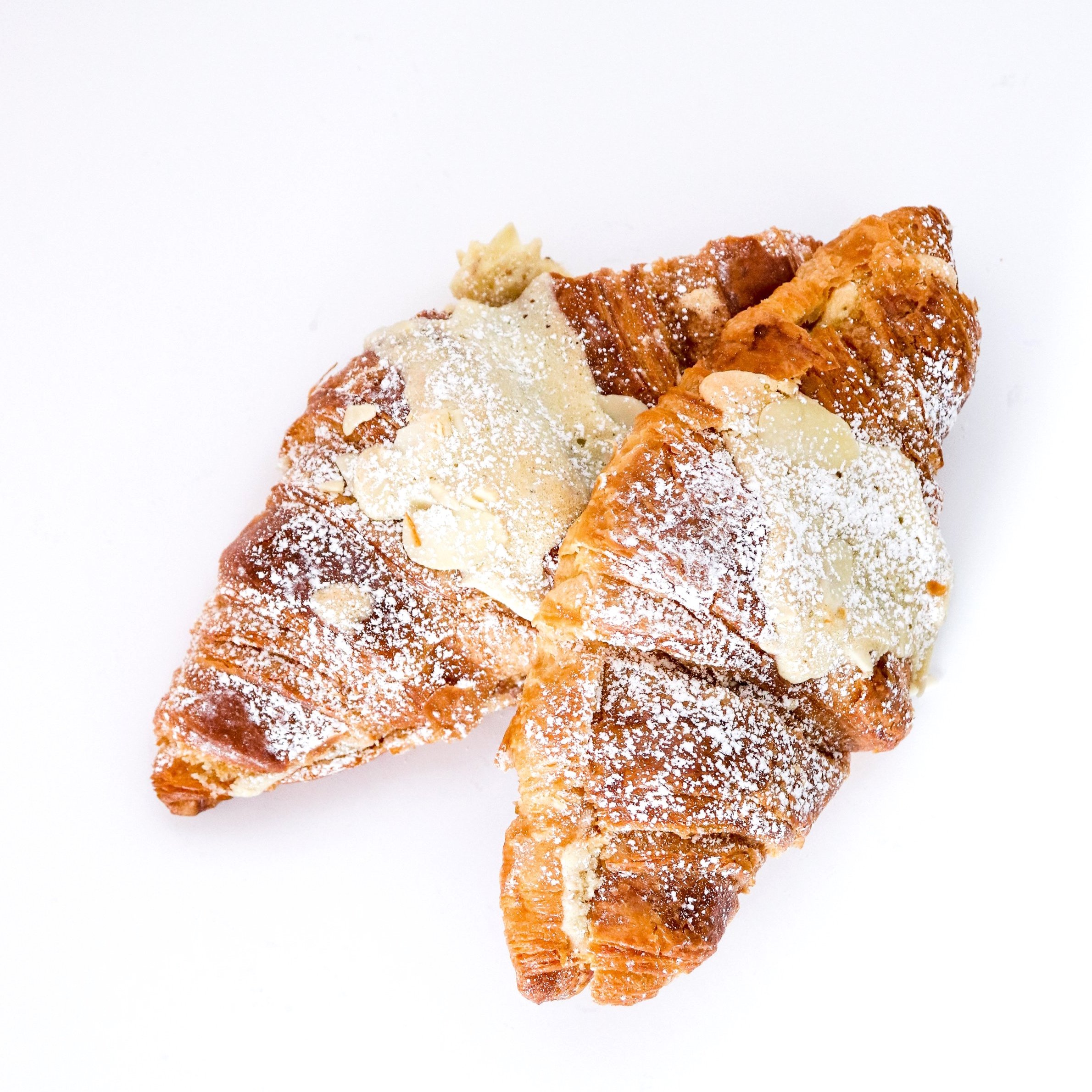Two croissants topped with almond slices and powdered sugar on a white background.