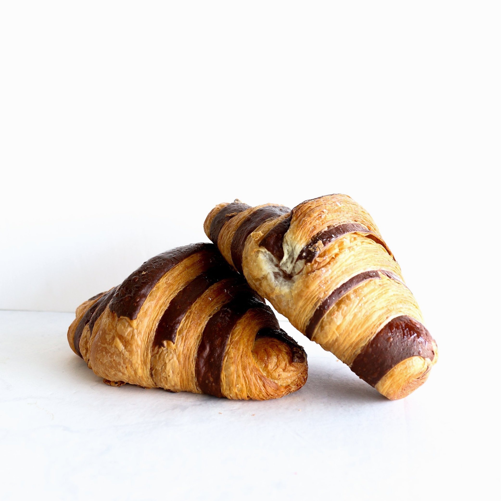 Two croissants with chocolate drizzle on a white surface against a white background.
