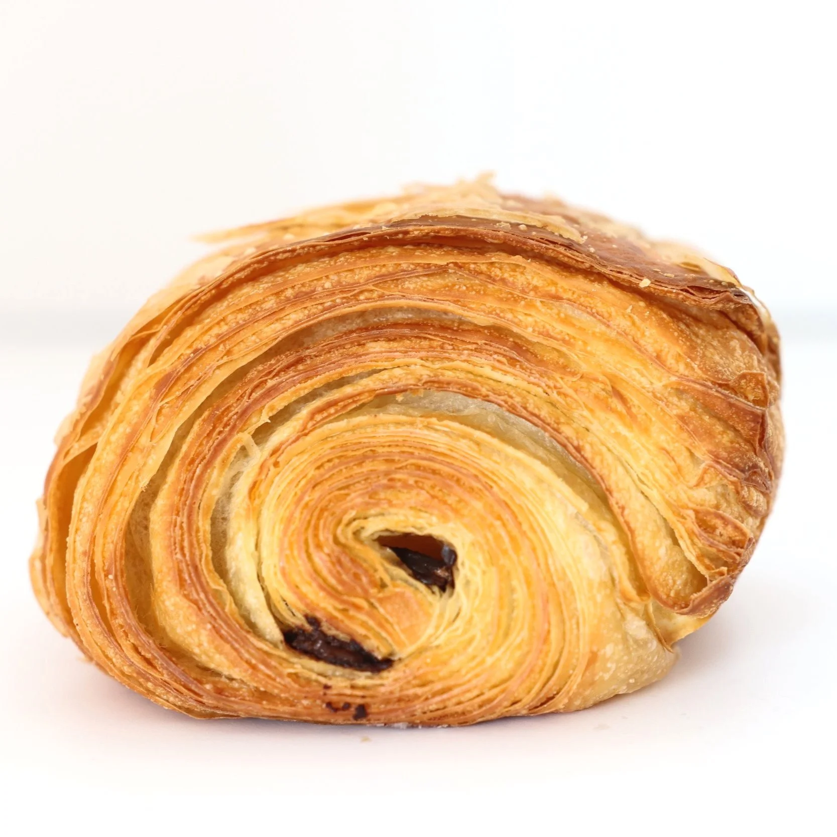 A close-up of a plain croissant with a flaky, golden-brown crust, placed on a white background.