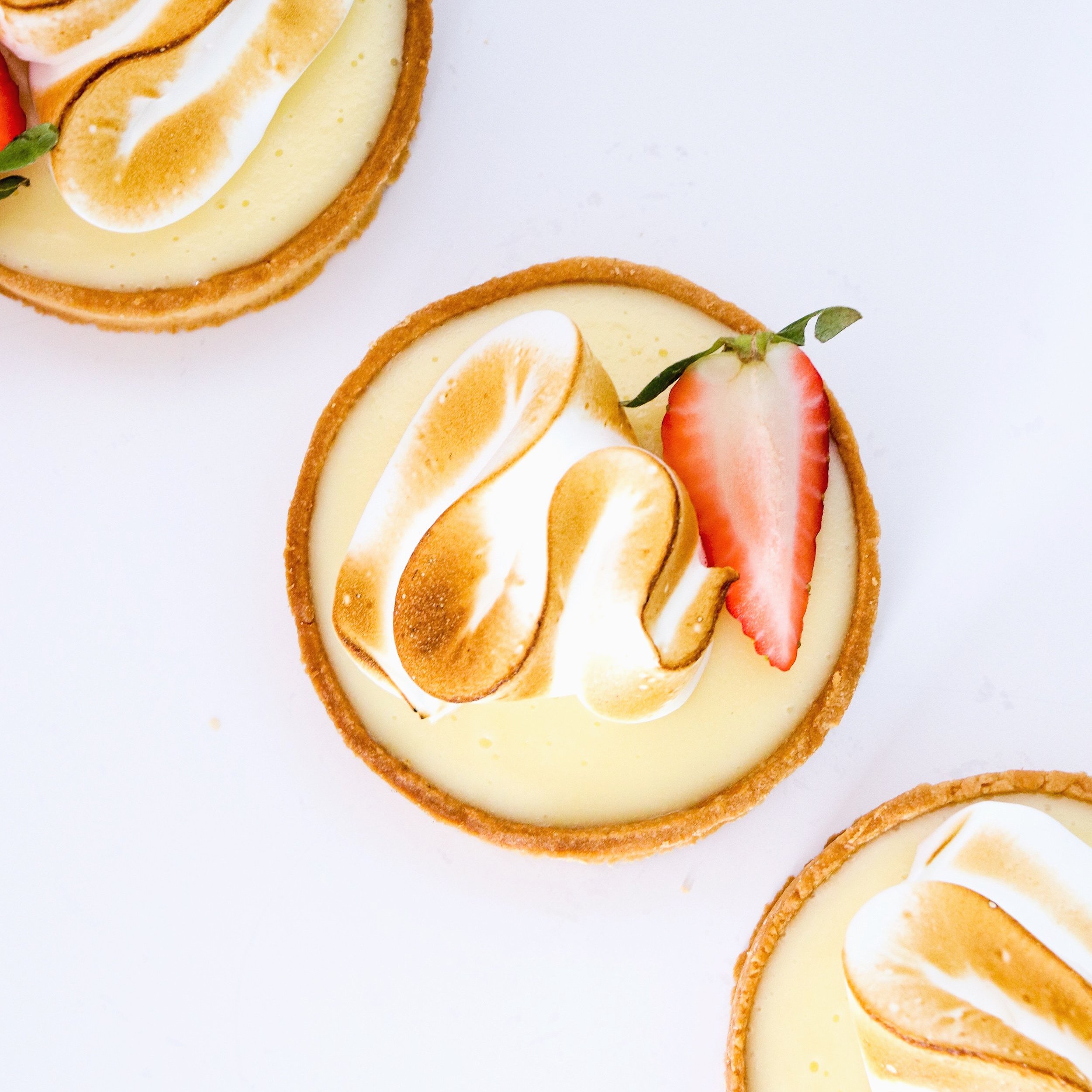 Close-up of a lemon tart with toasted meringue and a fresh strawberry slice on top.