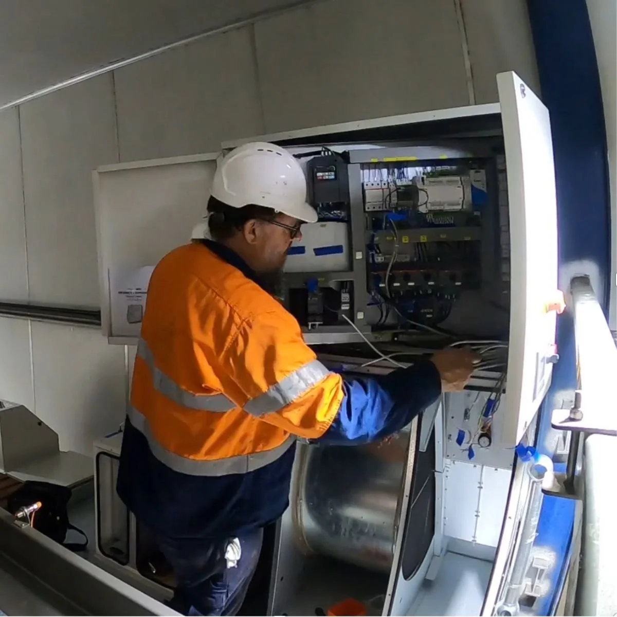 Humiscope technician performing electrical testing and preventative maintenance inside an industrial desiccant dehumidifier control cabinet in a meat processing facility