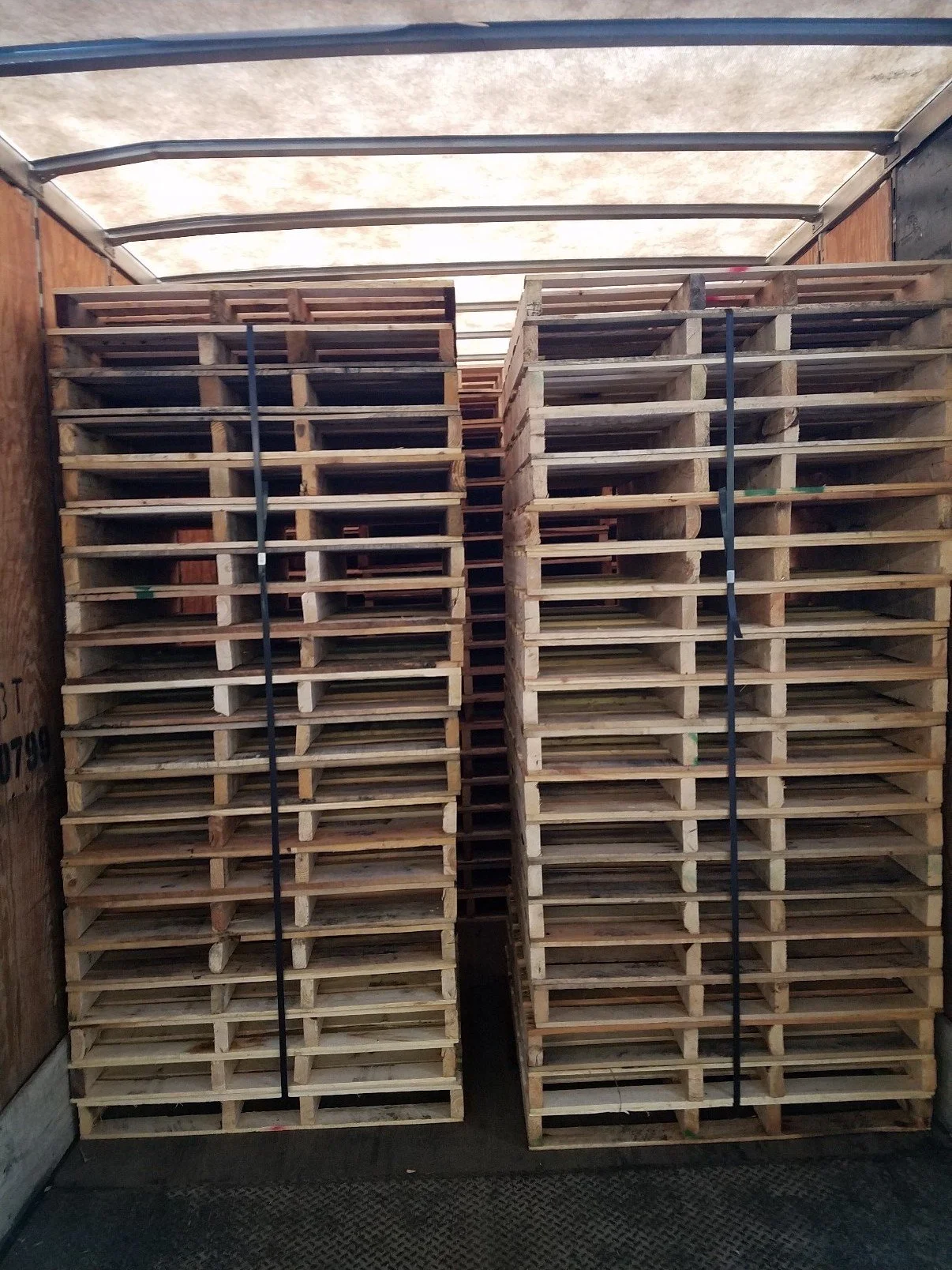 Pallets stacked inside a truck, secured with black straps.