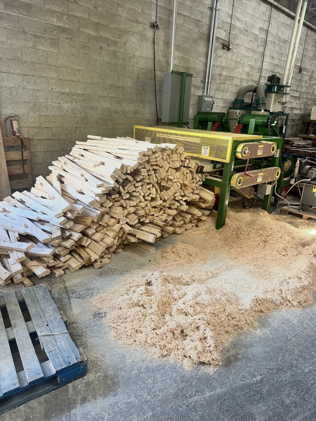 Stacked wood pieces and sawdust on the concrete floor of a woodworking shop.