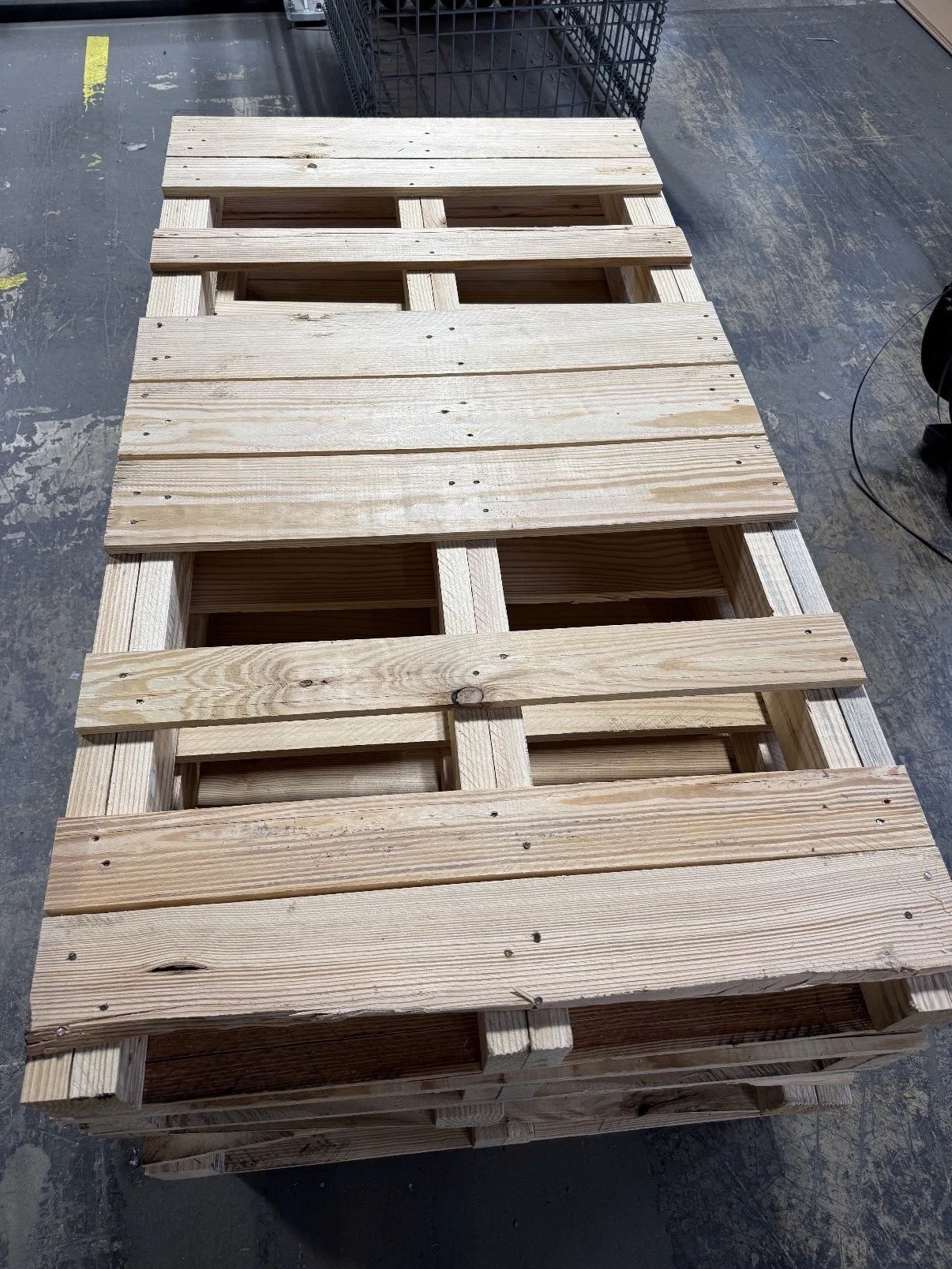 Wooden pallet on a workshop floor, with a black shopping cart in the background.