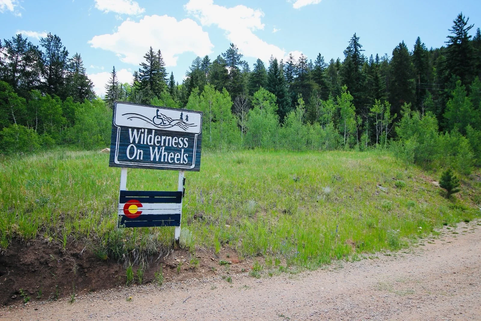photo of Wilderness On Wheels in the summer, showing the sign with the Wilderness On Wheels logo and Colorado flag!