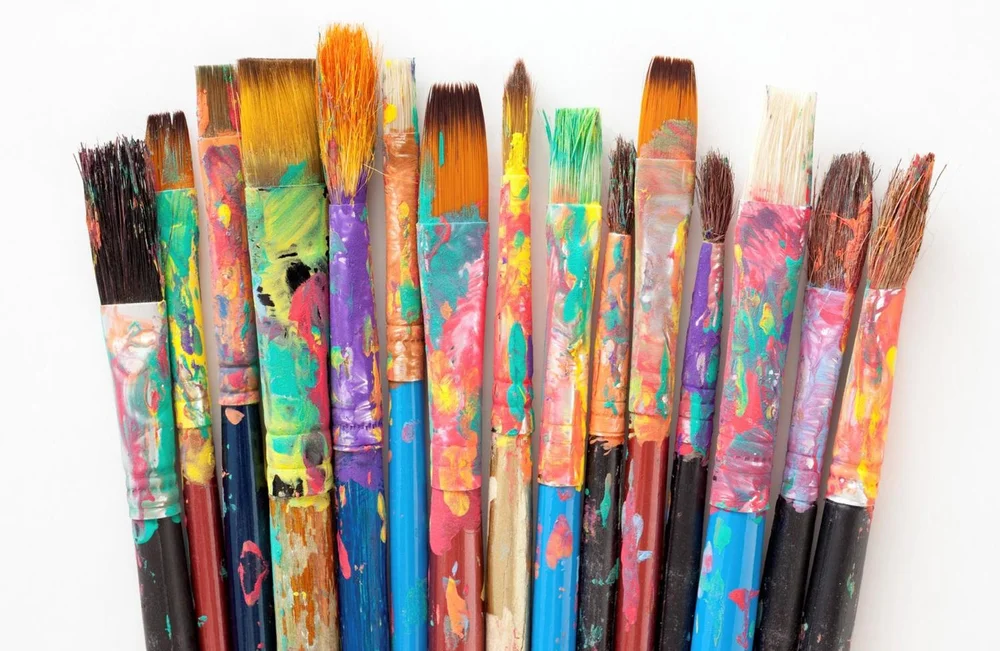 Paint brushes in a row covered with bright coloured paints.