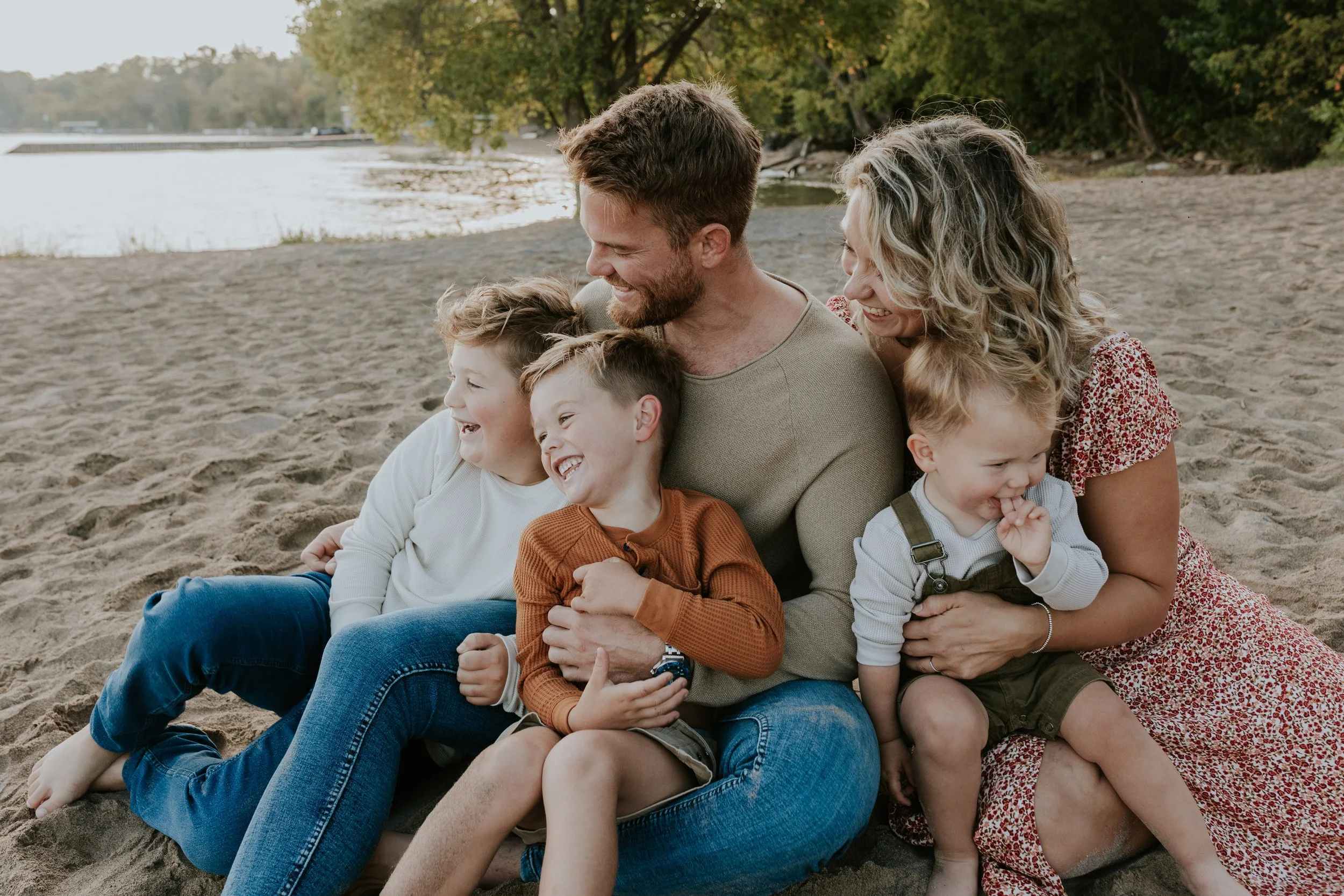 family of 5 sat together laughing and cuddling on the beach at de la salle beach in georgina ontario