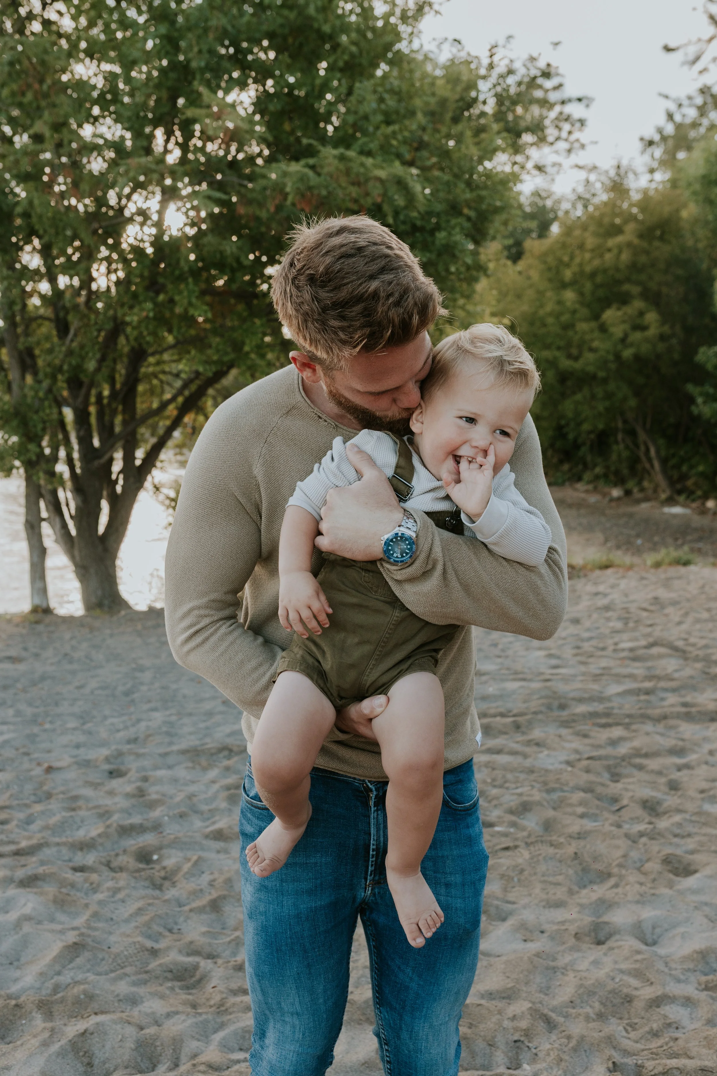 father holding young son who is laughing during family mini session at de la salle beach in georgina ontario