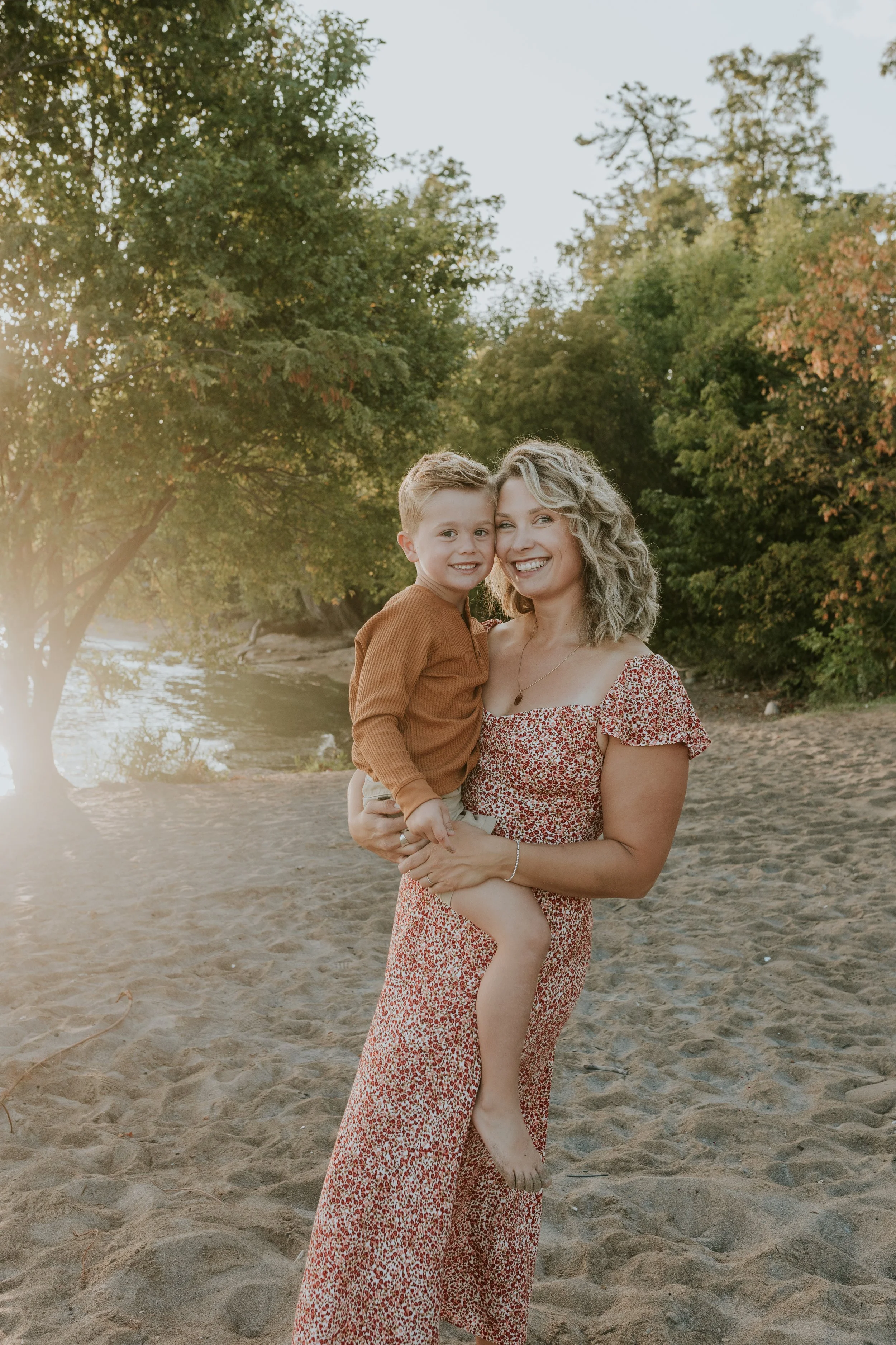 mother holding her son close with beautiful golden light during mini photo shoot at de la salle beach in georgina ontario
