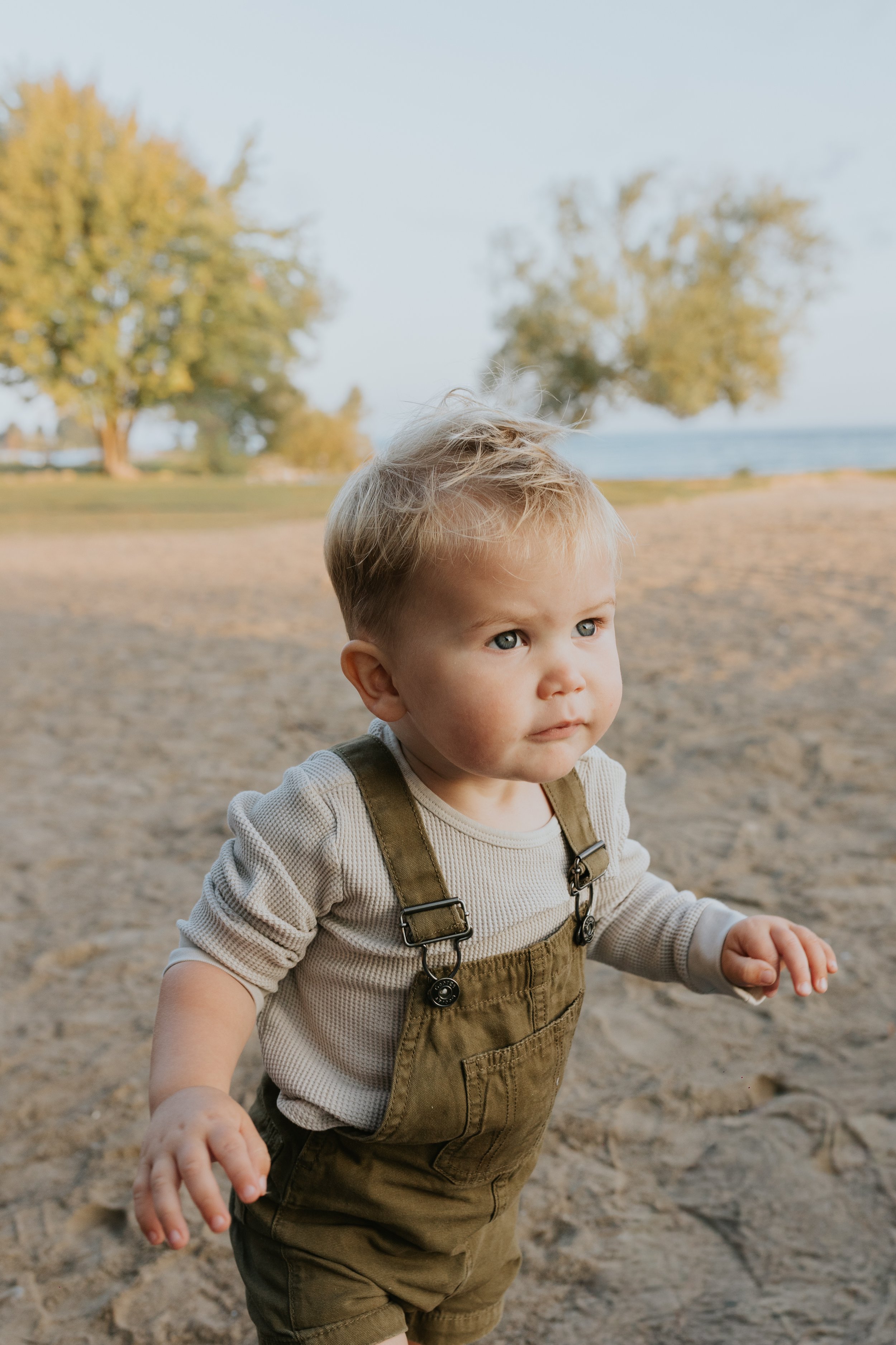 baby boy walking in the sand for family photos at de la salle beach in georgina ontario